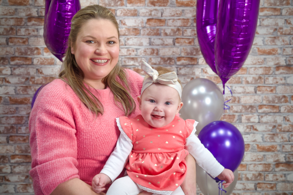 A mum holding a young girl with birthday balloons in the background