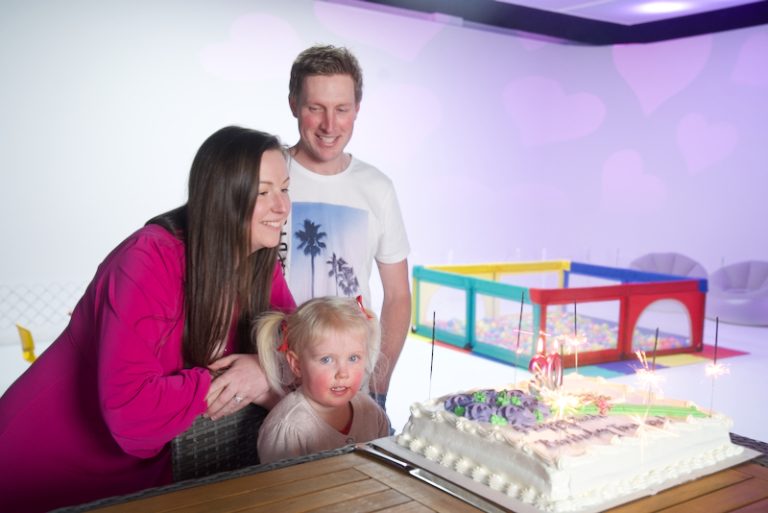 A mum and a dad standing and a young girl looking at a birthday cake