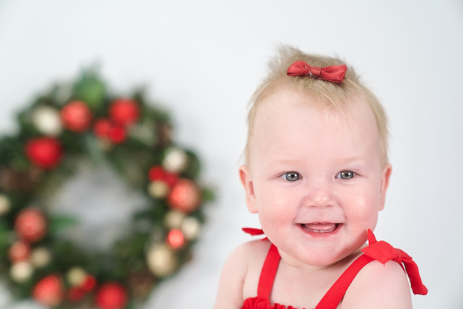 A young girl with a red bow in her hair and a Christmas wreath in the background